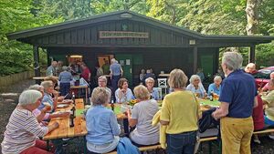 Personen tafeln an Tischen auf dem Vorplatz der Hütte.